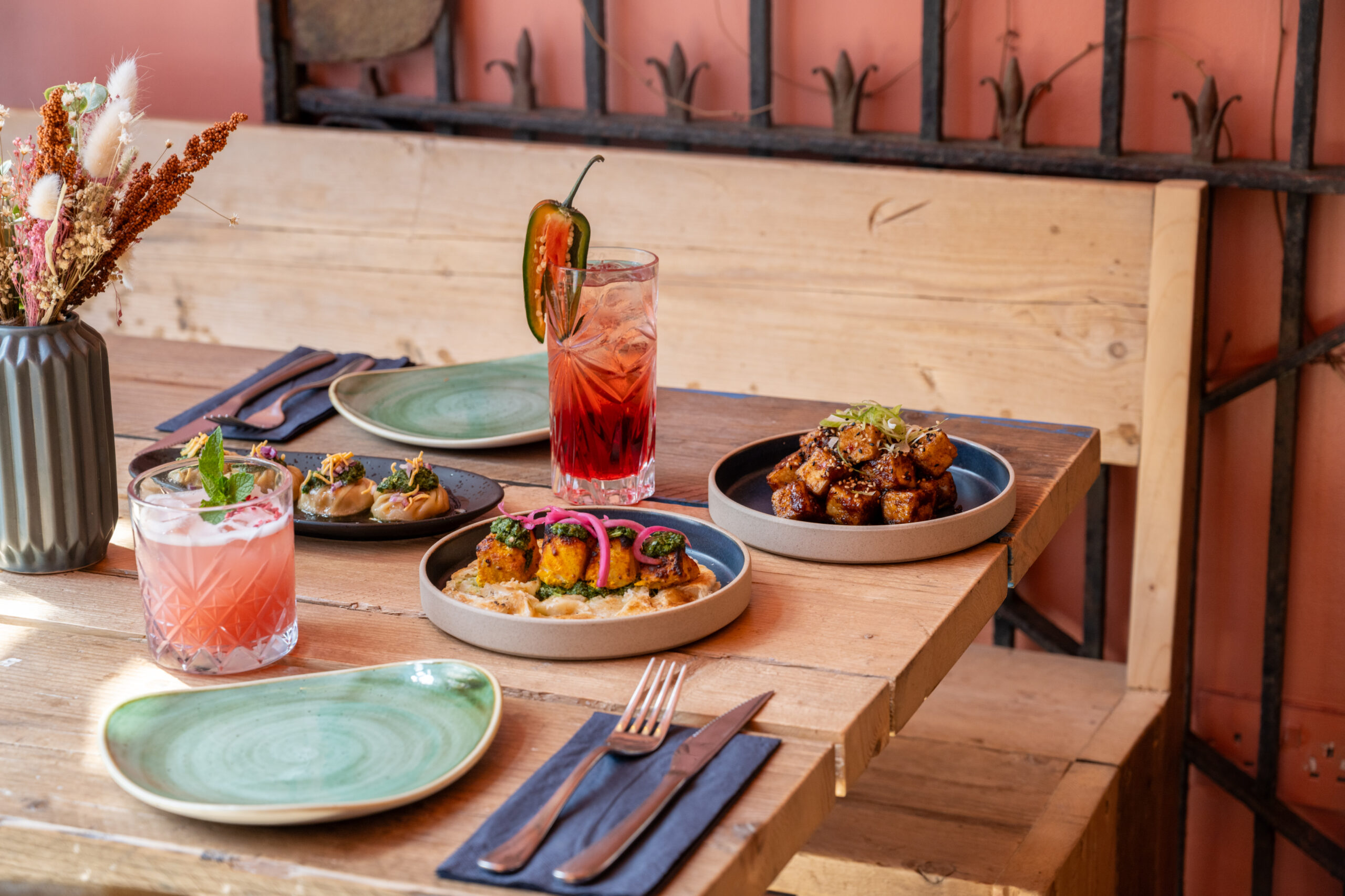 A cozy table setting with colorful cocktails and plated dishes in a rustic restaurant.