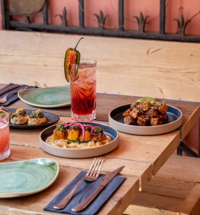 A cozy wooden table set with colorful plates and vibrant cocktails alongside delicious dishes.