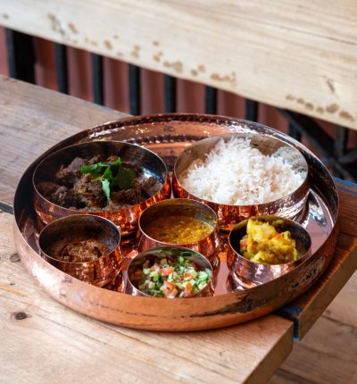 Traditional Indian thali with rice and assorted curries on a wooden table.