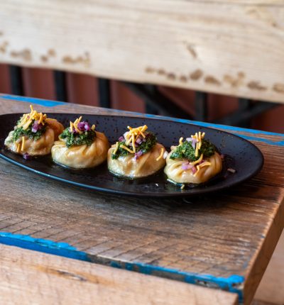 Elegant bite-sized appetizers garnished with herbs and edible flowers on a black platter.